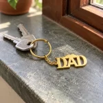 DAD Letter Keychain for Father’s Day in a golden finish, with keys on a stone windowsill