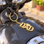 DAD Letter Keychain for Father’s Day in a golden finish, attached to a motorcycle ignition key