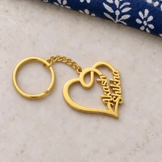 Heart Frame Couple Name Keychain in a golden finish, on a light stone display