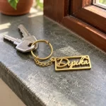 Heart Frame Personalized Name Plate Keychain in a golden finish, with keys on a stone windowsill