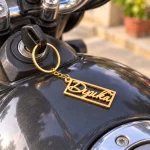 Heart Frame Personalized Name Plate Keychain in a golden finish, attached to a motorcycle ignition key