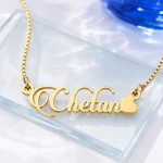 Gold-tone decorative script name necklace with a heart on a clear glass display
