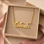 Gold-tone crown name necklace displayed in an open beige jewellery box