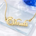 Gold-tone crown name necklace on a clear glass display