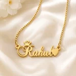 Gold-tone crown and heart name necklace on ivory satin