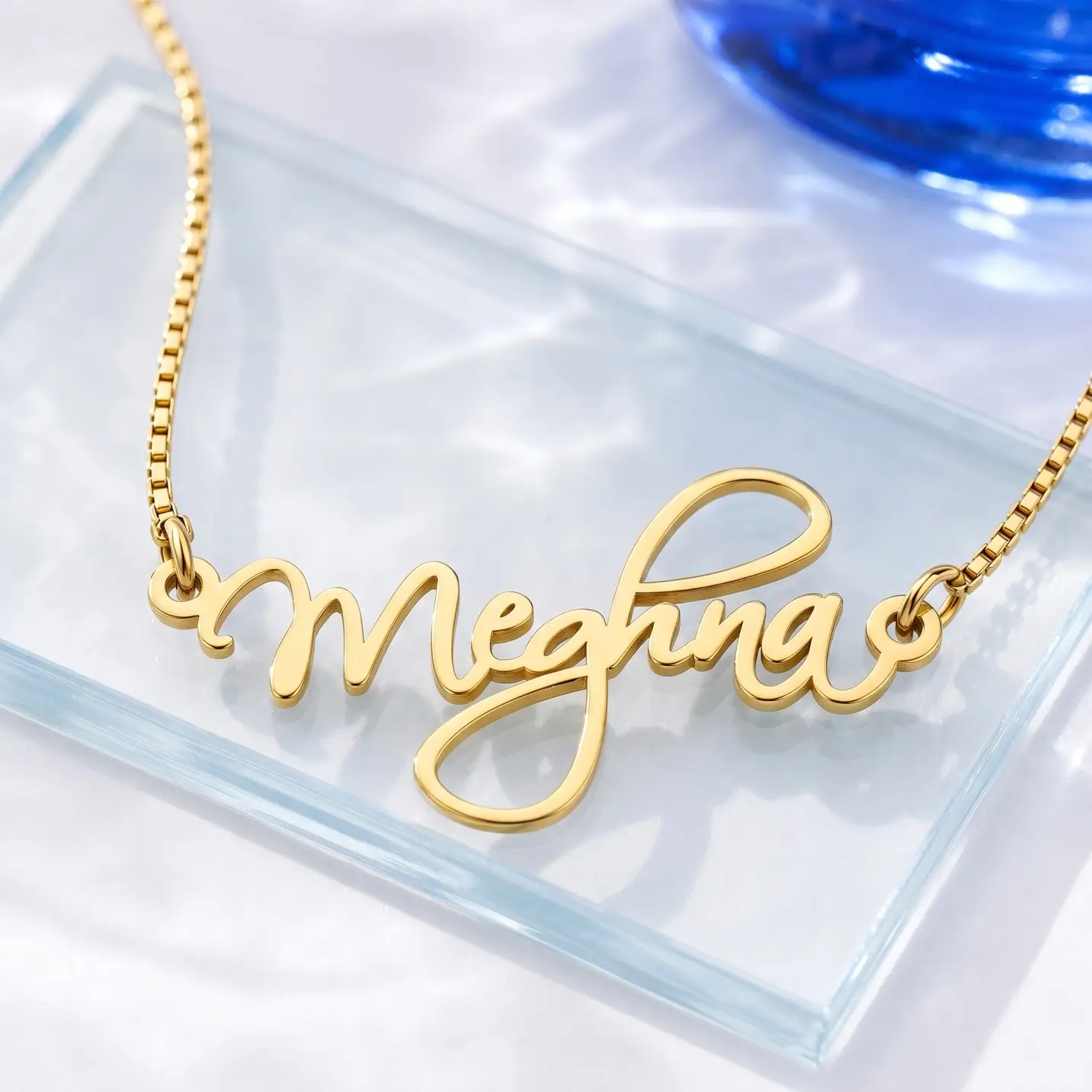 Curved Letter Name Necklace – Glass Display Gold-tone curved cursive name necklace on a clear glass display
