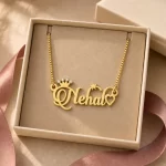 Gold-tone name necklace with a sparkling crown, star and heart displayed in an open beige jewellery box