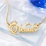 Gold-tone name necklace with a sparkling crown, star and heart on a clear glass display