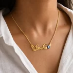 Gold-tone name necklace with a blue evil eye accent worn with a white blouse