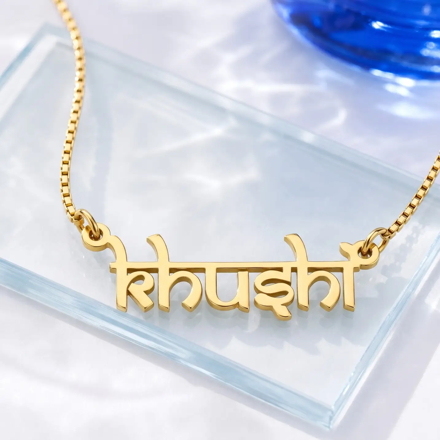Indian Style Name Necklace – Glass Display Gold-tone Indian style name necklace on a clear glass display