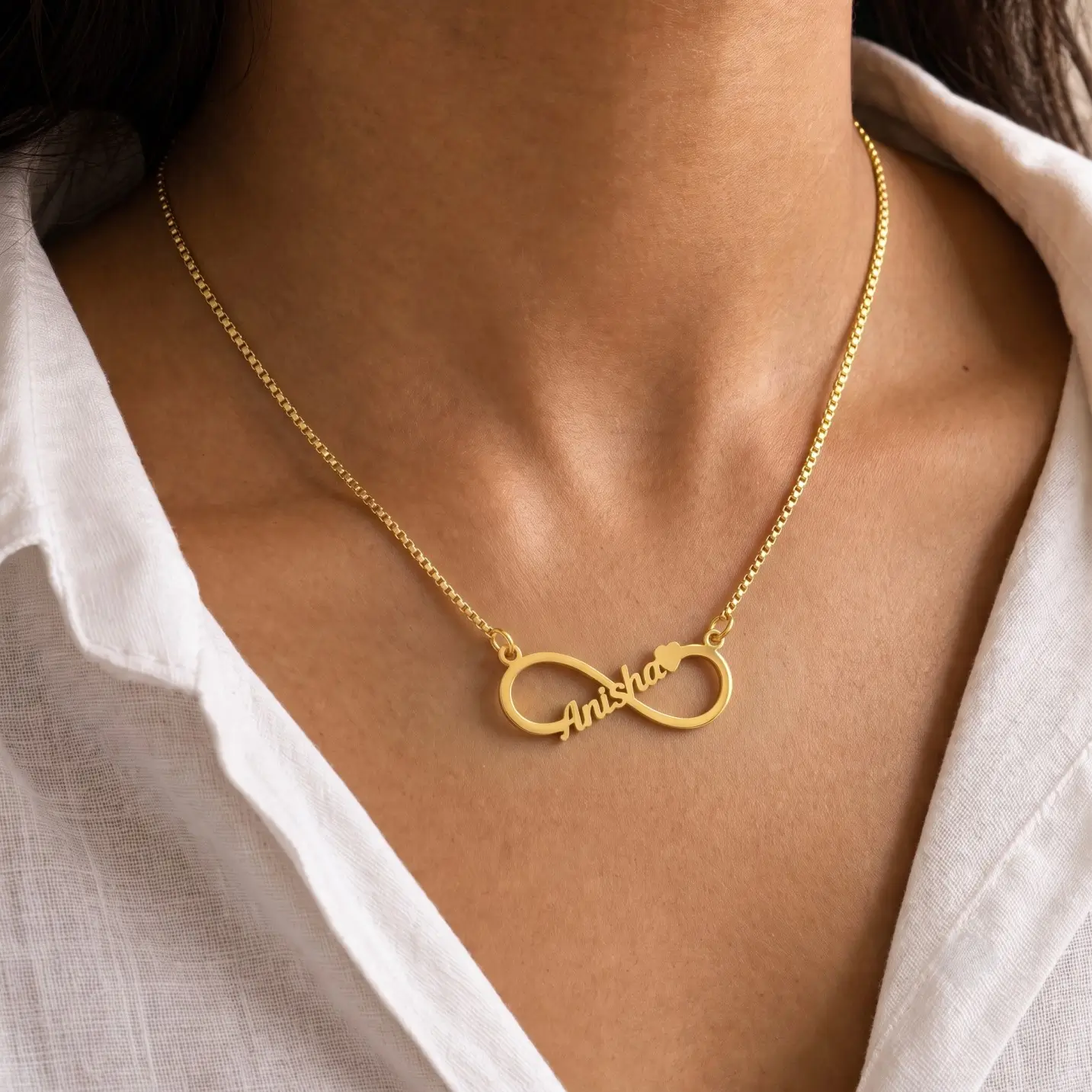 Personalized Infinity Name Necklace – Worn View Gold-tone infinity outline name necklace worn with a white blouse