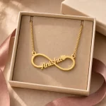 Gold-tone infinity outline name necklace displayed in an open beige jewellery box