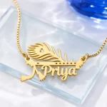 Gold-tone peacock feather and flute name pendant on a clear glass display
