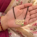 Red Rose Couple Name Necklace with a black-beaded chain held in a hand