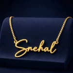 Gold-tone signature script name necklace on a navy velvet display
