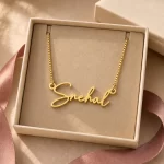 Gold-tone signature script name necklace displayed in an open beige jewellery box