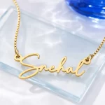 Gold-tone signature script name necklace on a clear glass display