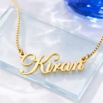 Gold-tone stylish cursive name pendant on a clear glass display
